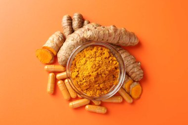 Kavanozda zerdeçal tozu, turuncu arka planda kök ve kapsüller.