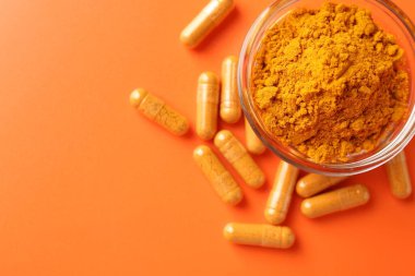 Turuncu arka planda kapsül ve kasede zerdeçal tozu, düz. Metin için boşluk