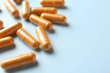 Açık mavi arka planda zerdeçal kapsülleri, yakın plan. Metin için boşluk