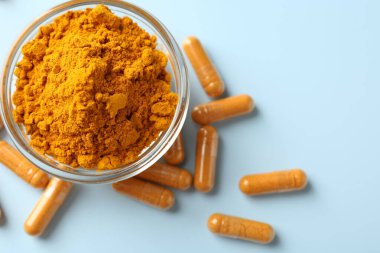 Açık mavi zemin üzerinde zerdeçal kapsülleri ve toz düz yatıyordu.