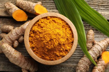 Tabaktaki zerdeçal tozu, kökler ve yapraklar ahşap masada, düz yerde.