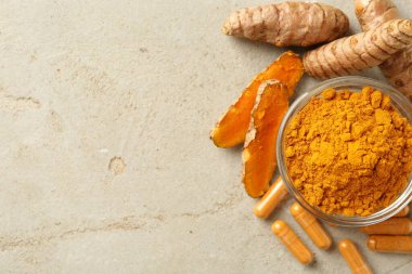 Zerdeçal kapsülleri, toz ve kökler gri masada, düz yerde. Metin için boşluk