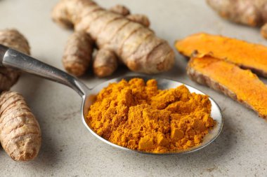 Kaşıkta Aromatik zerdeçal tozu ve açık gri masada taze kökler, yakın plan.