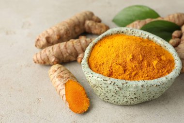 Kasede Aromatik zerdeçal tozu, taze kökler ve açık gri masadaki yapraklar, yakın plan.