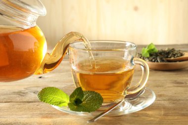 Çaydanlıktan cam fincana taze demlenmiş çay dökülüyor ahşap masada, yakın plan.