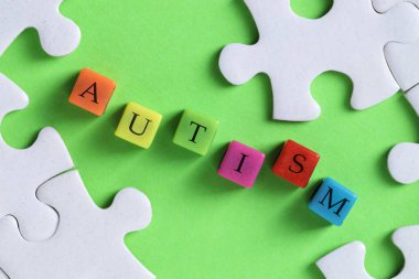 Renkli küplerden ve yeşil arkaplanda yapboz parçalarından oluşan kelime otizmi, düz yatıyordu