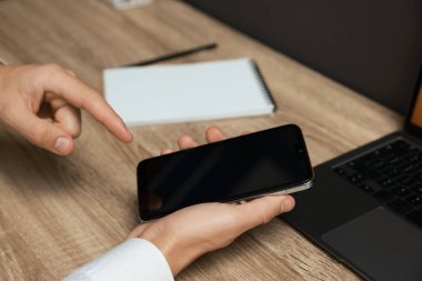Adam ahşap masada boş ekranlı akıllı telefon kullanıyor.