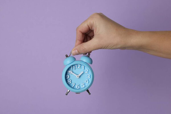 Woman with alarm clock on lilac background, closeup