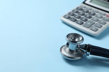 Açık mavi arkaplanda steteskop ve hesap makinesi, yakın plan. Metin için boşluk