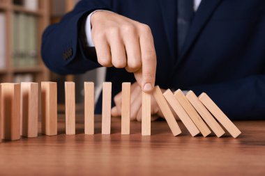 Domino etkisi. Masada tahta blokları iten adam, yakın plan.