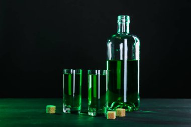 Siyah arka planda Absinthe shot bardakları, şişe ve esmer şeker
