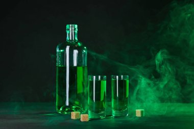 Absinthe shot bardakları, şişe ve esmer şeker siyah arka planda dumanlı