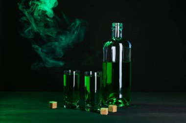 Absinthe shot bardakları, şişe ve esmer şeker siyah arka planda dumanlı