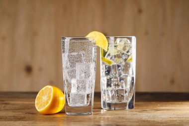 Soda suyunu bardaklarda buz küpleriyle tazelemek ve ahşap masada limon kesmek, yakın plan.