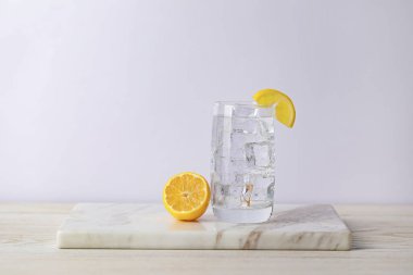 Soda suyunu bardakta buzla tazelemek ve ahşap masada limon kesmek.