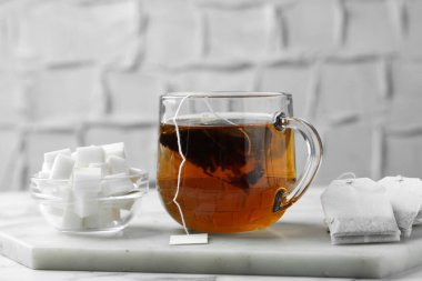 Cam bardakta çay poşeti, sıcak içecek ve şeker küpleri açık mermer masada, yakın plan.