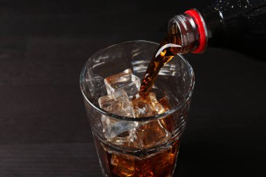 Siyah ahşap masada şişeden cama ferahlatıcı kola dökülüyor, yakın plan.