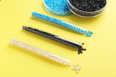 Petri kabında renkli plastik granüller ve sarı arka planda test tüpleri, yakın plan.