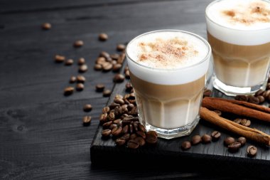 Bardakta latte macchiato, kahve çekirdekleri ve siyah ahşap masada tarçın, yakın plan. Metin için boşluk
