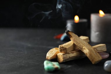 Yanan palo santo çubuğu, değerli taşlar ve siyah masada yanan mumlar, yakın plan. Metin için boşluk