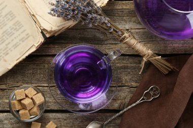 Cam fincanda Aromatik lavanta çayı, kaşık, kahverengi şeker, çaydanlık, kitap ve bir demet kuru çiçek ahşap masa, düz uzanmış