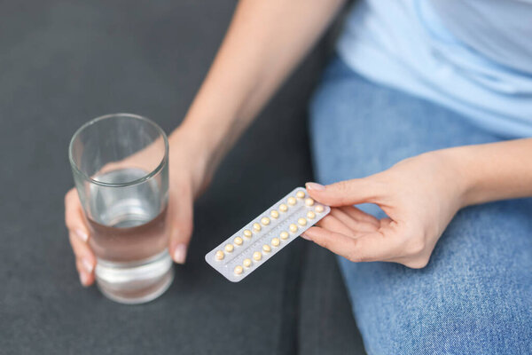 Woman with contraceptive pills and glass of water on sofa, closeup