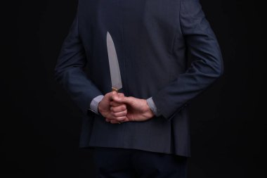 Siyah arka planda sırtında bıçak tutan bir iş adamı, yakın plan.