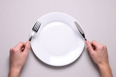 Çatal bıçaklı ve temiz tabaklı bir adam açık gri masada, üst tarafta.