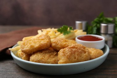 Lezzetli tavuk nugget ve ahşap masada soslu patates kızartması, yakın plan.