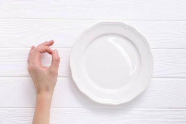 Beyaz ahşap masadaki boş tabağın yanında iyi niyet gösteren bir kadın.