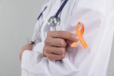 Çoklu Skleroz farkındalığı. Açık gri arka planda turuncu kurdeleli doktor, yakın plan.