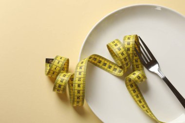 Bulimia. Bej arka planda çatal ve mezura ile plaka, üst görünüm
