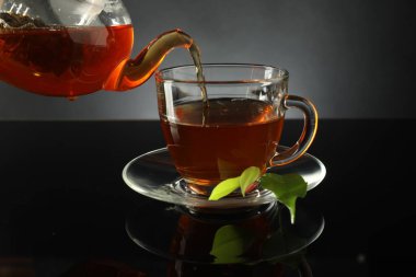 Çaydanlıktan taze demlenmiş çayı siyah masaya, cam fincana dökerek.