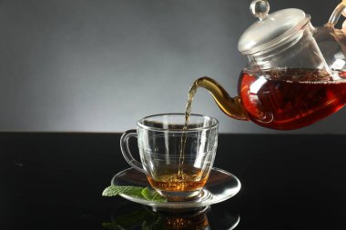 Koyu ayna masasında çaydanlıktan fincana taze demlenmiş çay dökülüyor.