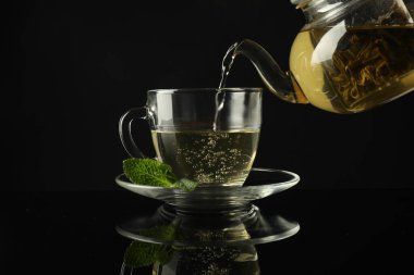 Koyu ayna masasında çaydanlıktan fincana taze demlenmiş çay dökülüyor.