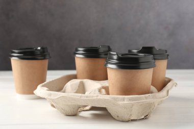 Kağıt kahve bardakları beyaz ahşap masadaki karton tutacakta, yakın plan.