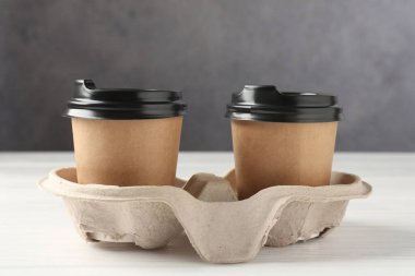 Kağıt kahve bardakları beyaz ahşap masadaki karton tutacakta, yakın plan.