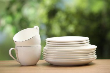 Temiz bulaşık takımları ve bardaklar ahşap masada bulanık yeşil arka plana karşı