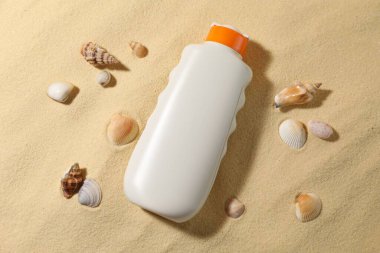 Bir şişe güneş koruması ürünü ve kumdaki deniz kabukları.