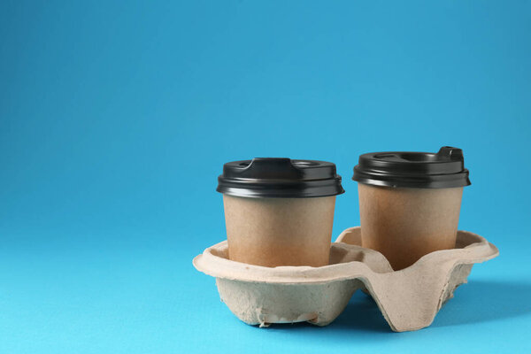 Paper coffee cups in cardboard holder on light blue background. Space for text
