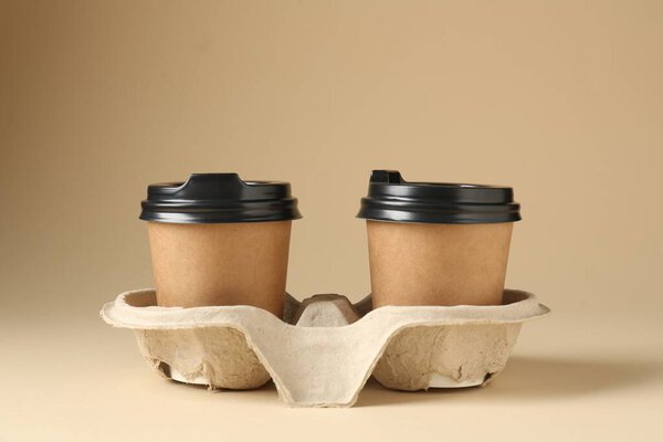 Paper coffee cups in cardboard holder on beige background