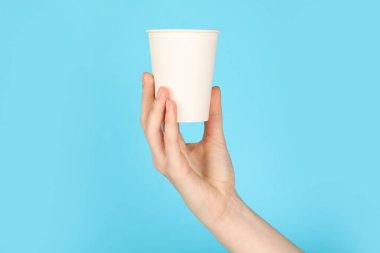 Açık mavi arka planda kağıt bardak tutan kadın, yakın plan. Tasarım için model