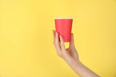 Sarı arka planda kağıt bardak tutan kadın, yakın plan. Tasarım için model