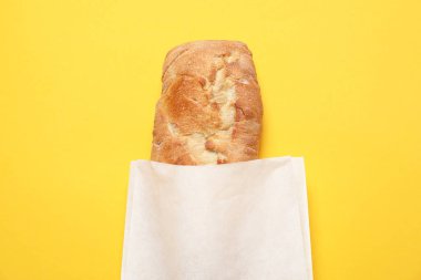 Sarı arka planda taze ekmekli kağıt torba, üst manzara.