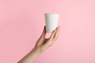 Pembe arka planda kağıt bardak tutan kadın, yakın plan. Tasarım için model