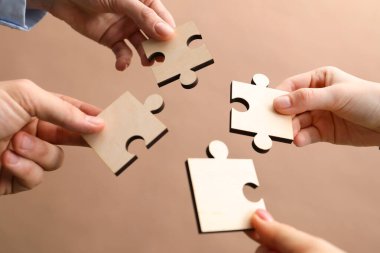 Takım çalışması. Bej arkaplan üzerine yapboz parçaları koyan bir grup insan, yakın plan