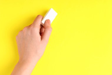 Sarı arka planda silgi kullanan bir kadın, yakın plan. Metin için boşluk