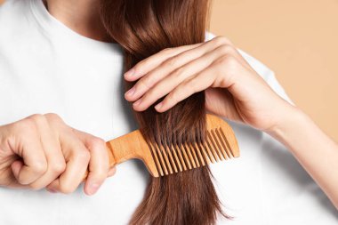 Bej arka planda saçını tarayan kadın, yakın plan.