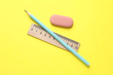 Sarı arkaplanda silgi, kalem ve cetvel, üst görünüm