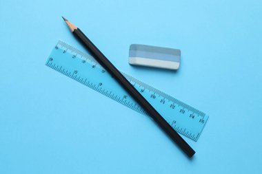 Açık mavi arkaplanda silgi, kalem ve cetvel, üst görünüm